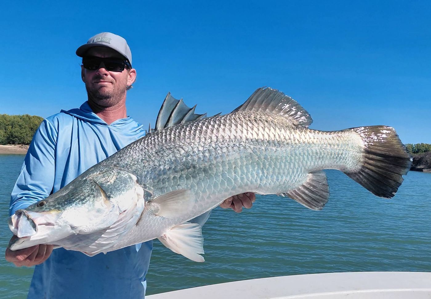 Big barramundi held up against a clear blue sky