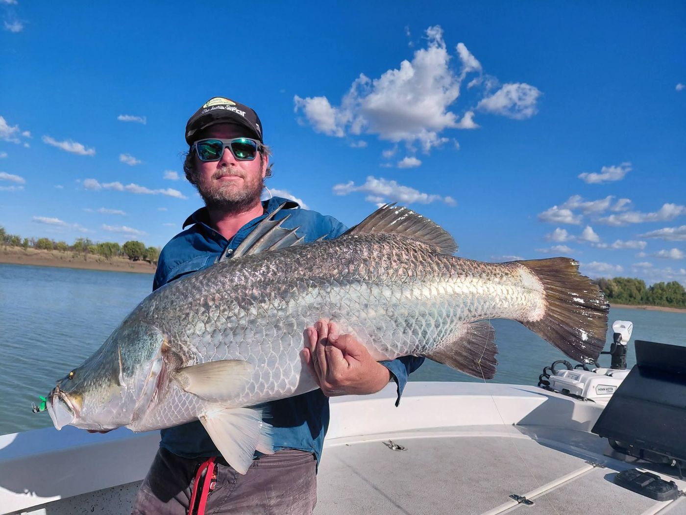 Angler at the bow holding a big barramundi, with the sonar screen and electric motor behind him