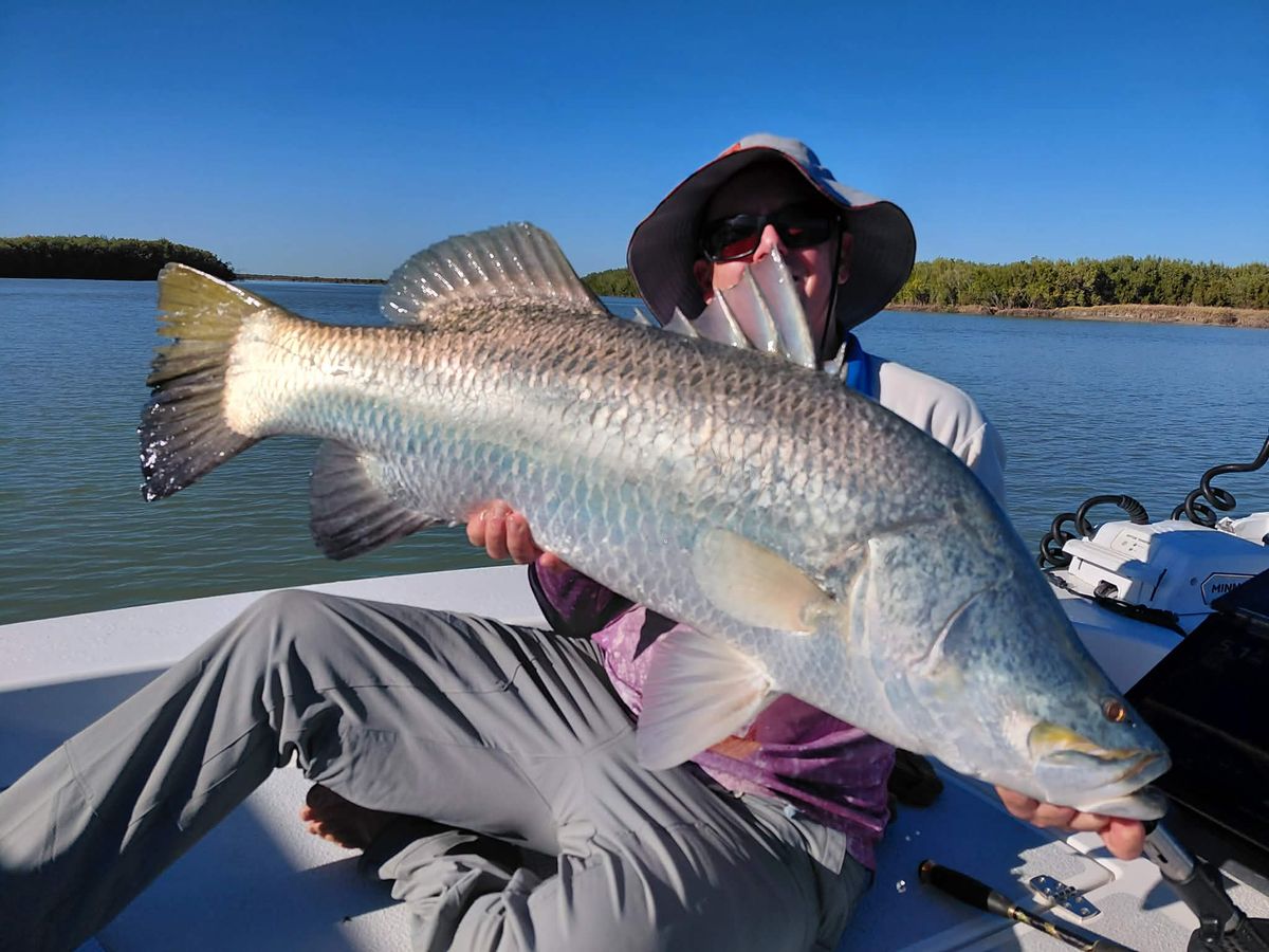 Seated angler holding a long barramundi across the deck